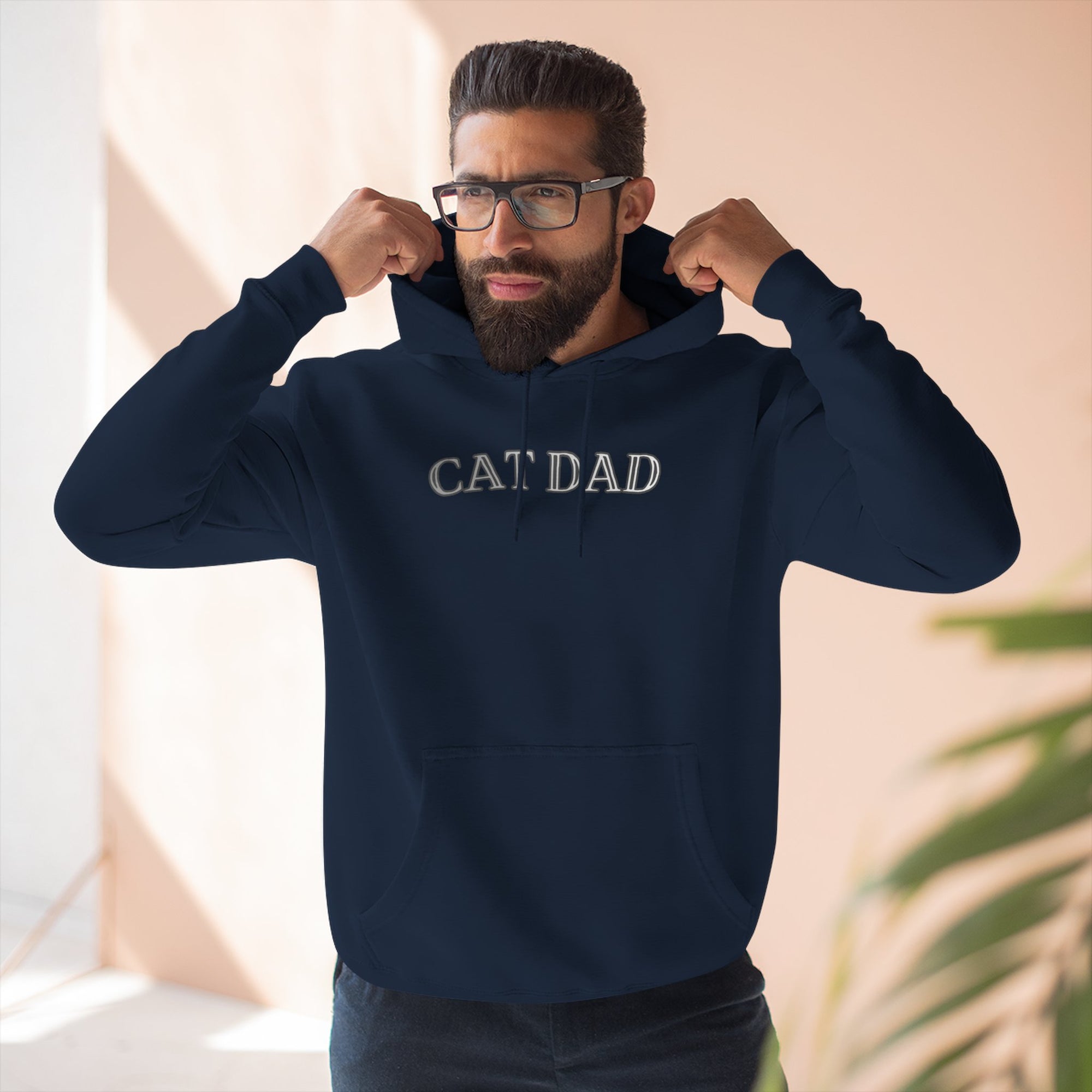 Man wearing a navy blue hoodie with 'CAT DAD' text, standing indoors.