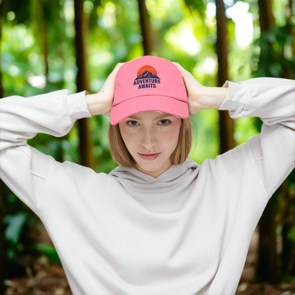 Person wearing a pink cap with 'Adventure Awaits' text and a mountain graphic on a white background